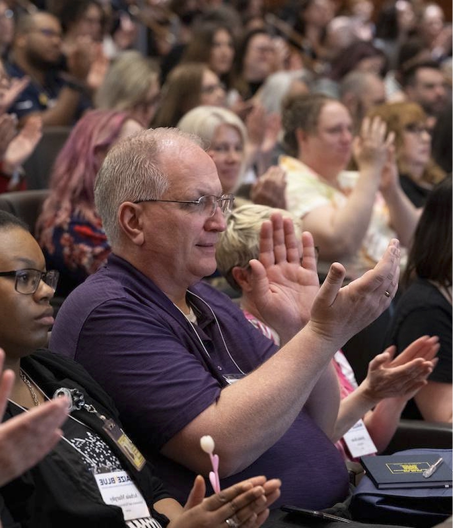 A large group of people sitting in rows at an event, applauding enthusiastically.