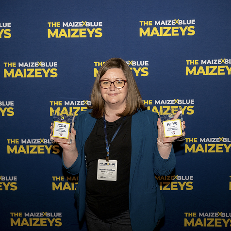 A woman holding two Maizey awards in front a Maizey branded backdrop.
