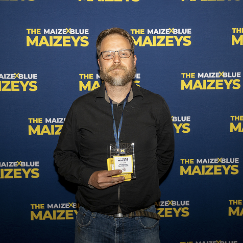 A man holding a Maizey award in front a Maizey branded backdrop.