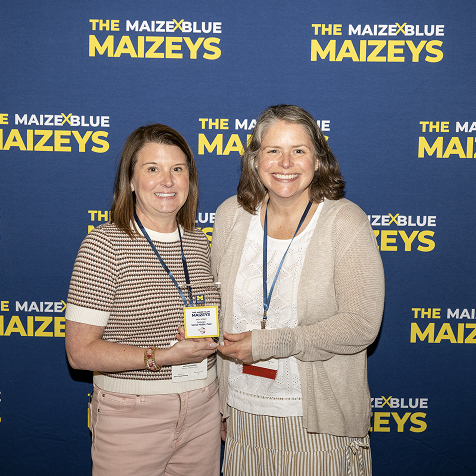 Two women holding a Maizey award in front a Maizey branded backdrop.